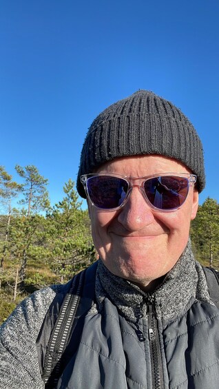 A person wearing a beanie and sunglasses, standing outdoors with trees in the background. 5