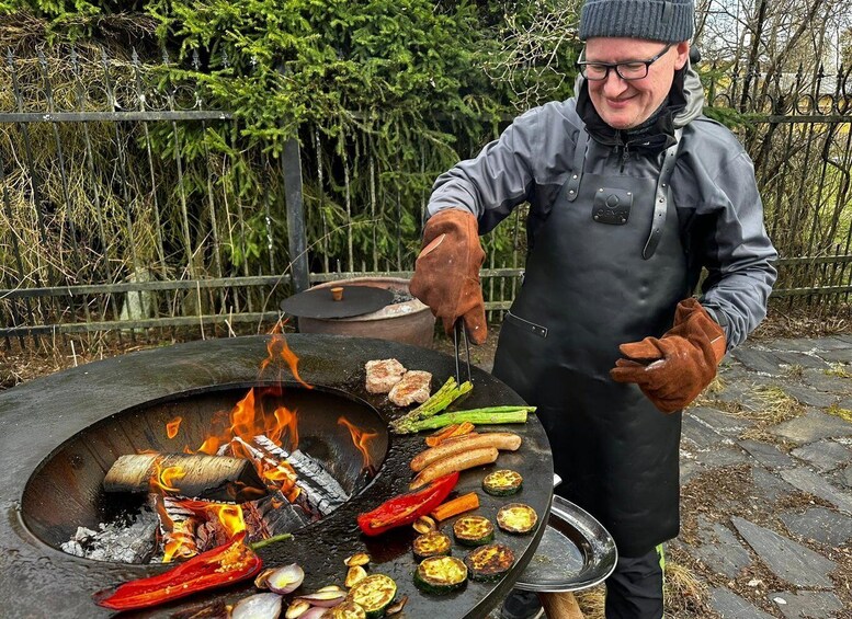 A person grilling various vegetables and sausages on an outdoor grill. 1