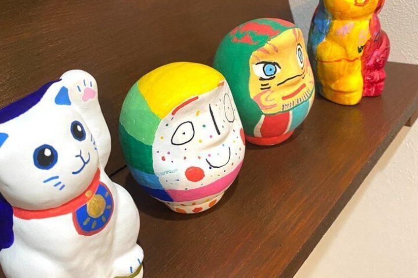 Three painted ceramic figurines on a wooden shelf. 4