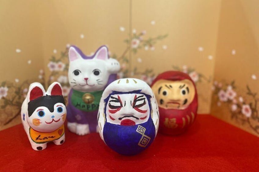 A collection of Japanese dolls on a red surface with a floral backdrop. 1