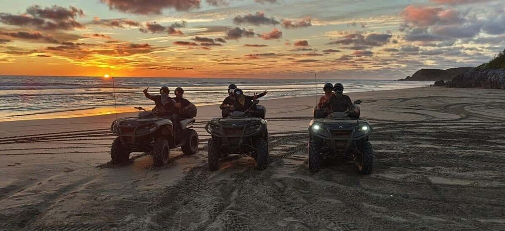 Three off-road vehicles on a beach at sunset. 1