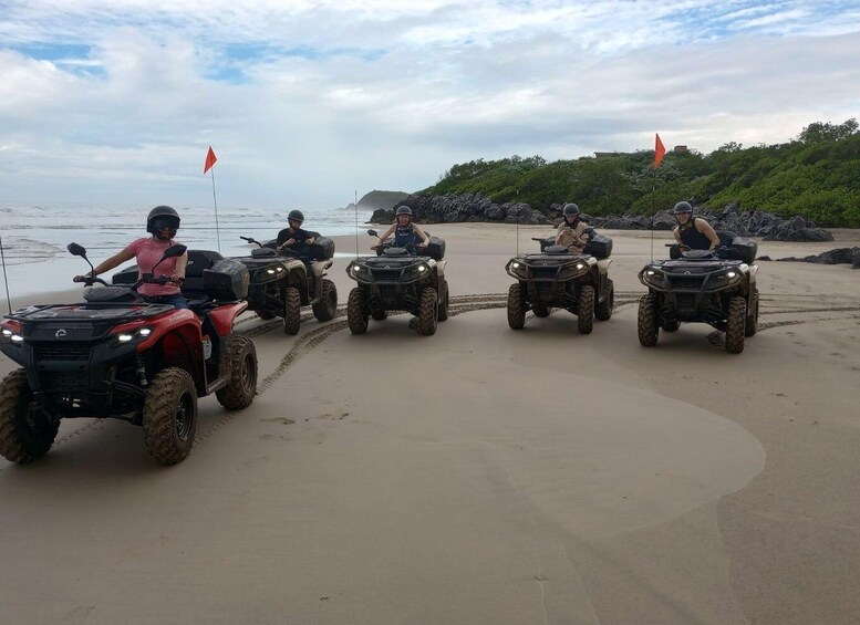 Four all-terrain vehicles on a sandy beach with ocean in the background. 2