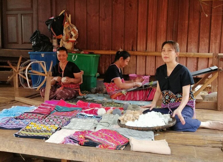 Women working with textiles, possibly weaving or crafting, in a rustic setting with wooden walls and a table displaying colorful fabrics. 4