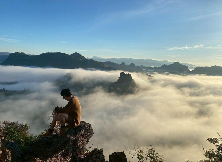 A person sitting on a rock overlooking a valley with mist-covered mountains. 1