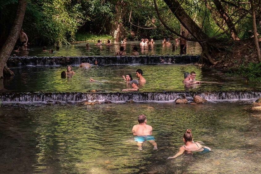 A natural hot spring with multiple levels of water and people swimming and relaxing. 3