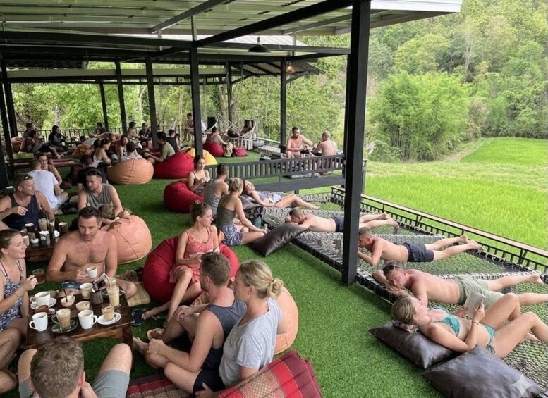 A group of people relaxing on grass and bean bags under a covered area with a view of a green landscape. 4