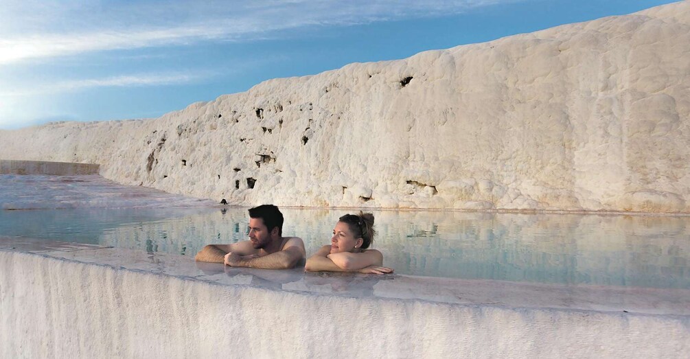 Two people relaxing in a natural hot spring with mineral deposits around. 3