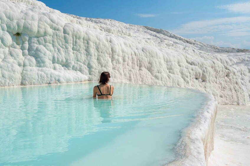 A person in a natural pool surrounded by white travertine terraces. 1