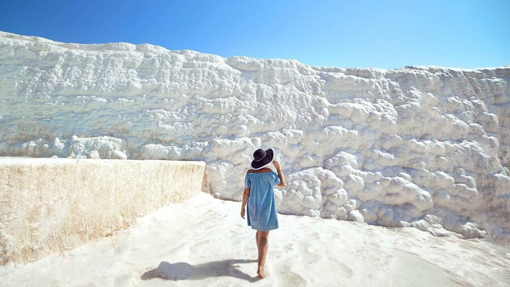 A person standing on a sandy beach with white, textured rock formations in the background. 2