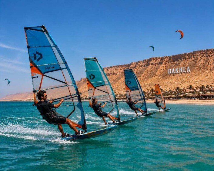 Windsurfers on a calm sea with clear skies and a mountainous backdrop. 4