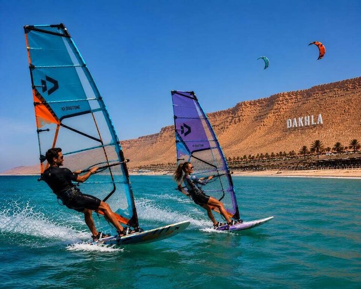 Two people windsurfing on turquoise water with a mountainous landscape in the background. 5