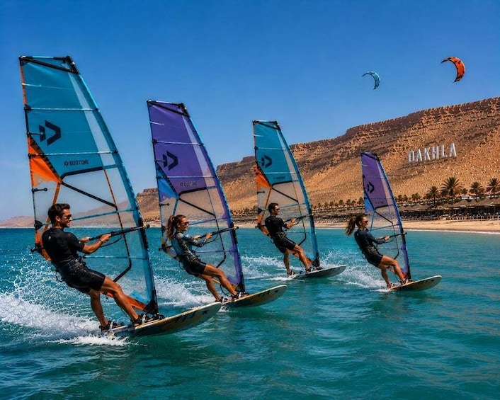 Three people windsurfing on a calm sea with clear skies and a mountainous backdrop. 2
