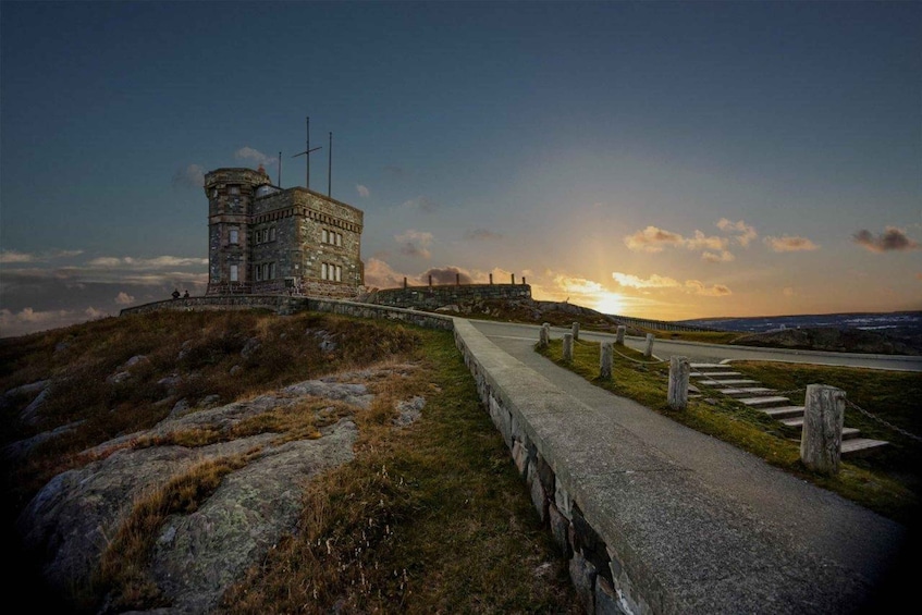 A stone tower with a flagpole, a paved path, and a sunset in the background. 2
