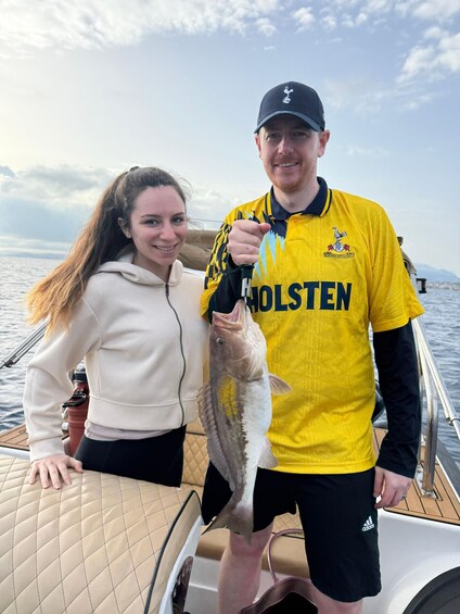 Two people on a boat holding a fish. 2