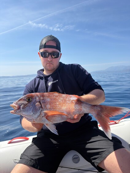 A person holding a fish on a boat with a clear sky and calm sea in the background. 4