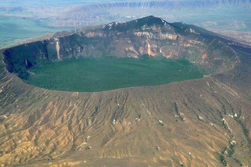 A large crater with steep walls and a green center, surrounded by barren land. 1