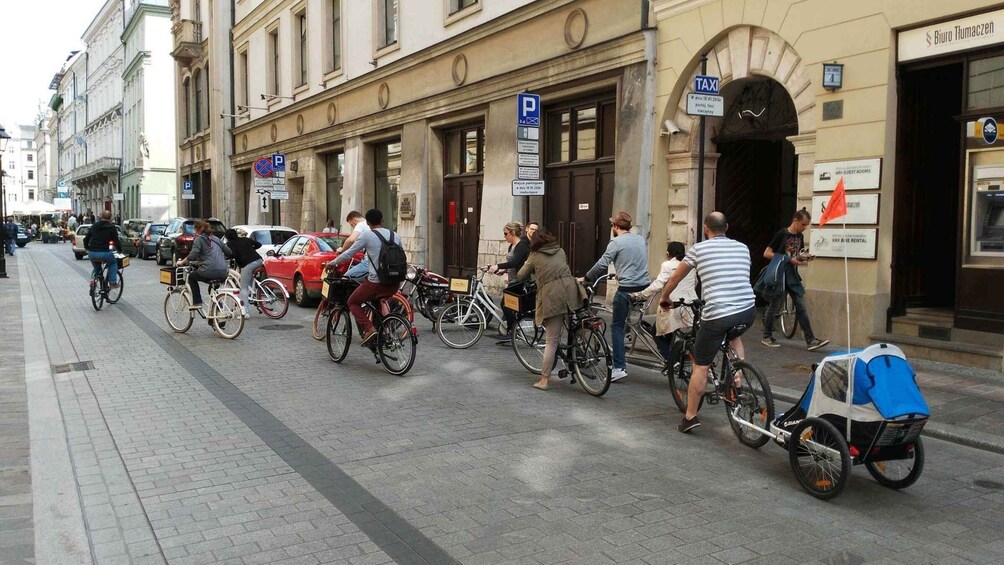 Katukuva, jossa näkyy pyöräilijöitä, punainen auto ja rakennus, jossa on kyltti, jossa lukee ”Biuro Tłumaczenia”. 2