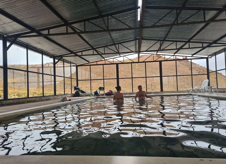 An indoor swimming pool with people in the water, surrounded by a metal roof and large windows. 2