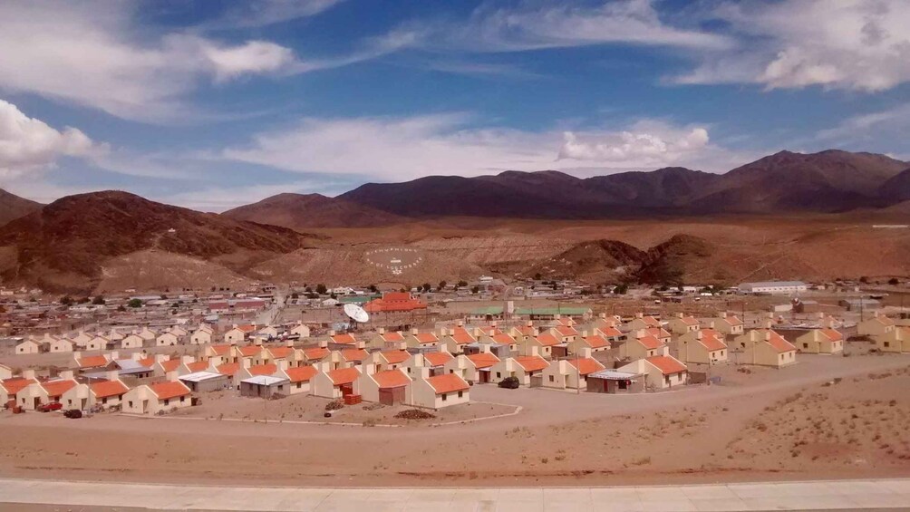 A town with red-roofed houses, a satellite dish, and mountains in the background. 5