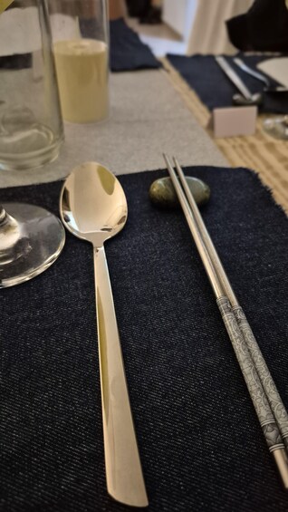 A spoon, chopsticks, and a glass on a dark fabric surface. 1