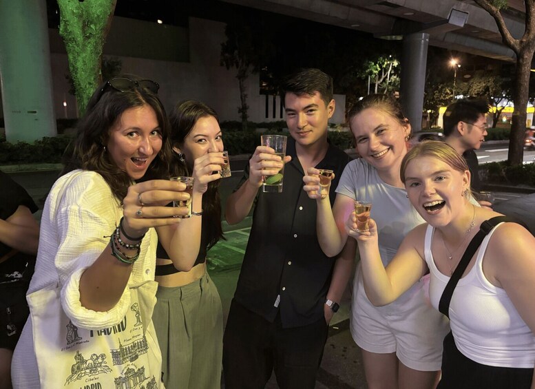 A group of people holding drinks, standing outdoors at night. 1