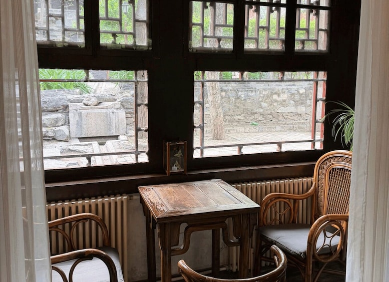 A rustic wooden table and chairs by a stone wall, with a view of greenery outside. 5