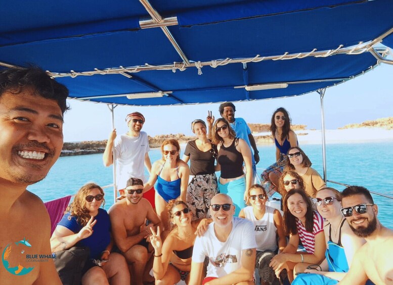 A group of people on a boat with a blue canopy, surrounded by water and rocky coastline. 2