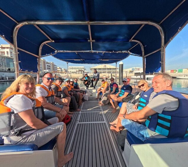 A group of people on a boat with life jackets, a covered deck, and a cityscape in the background. 1