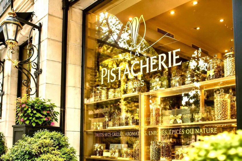 A storefront with a sign reading 'LA PISTACHERIE PARIS' and shelves of jars with nuts and dried fruits. 5