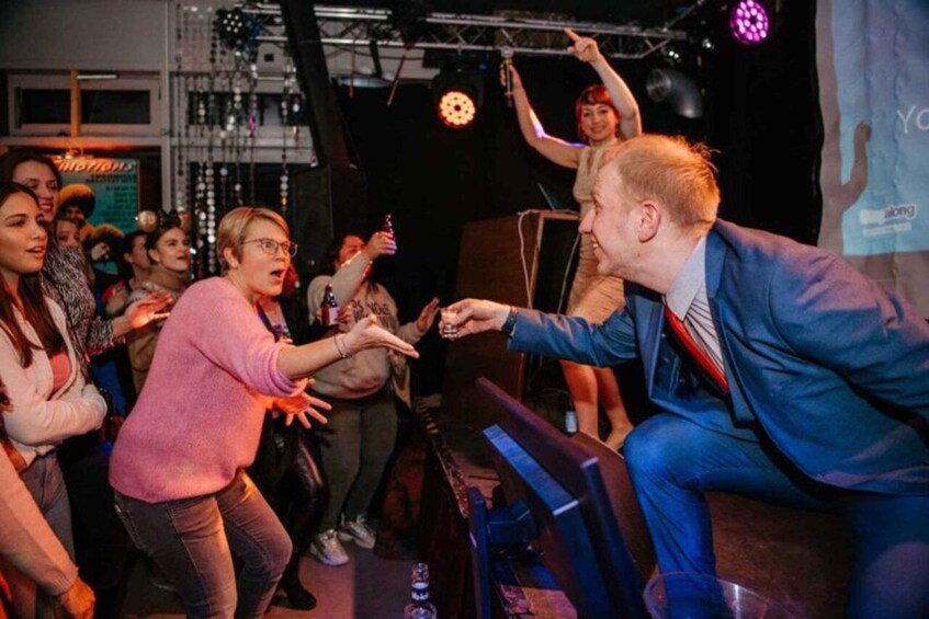 A person in a blue suit seated on a stage with a microphone, surrounded by a crowd. 2