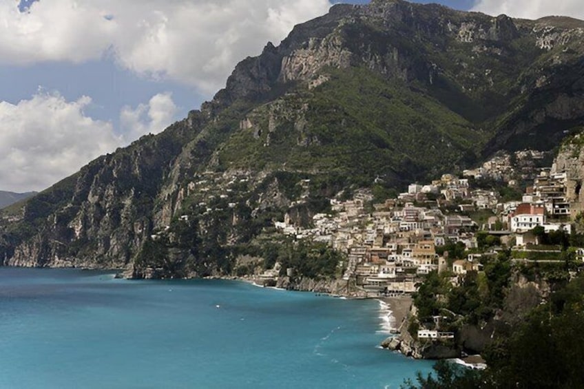 A coastal town nestled against a mountainous backdrop with a clear blue sea. 2