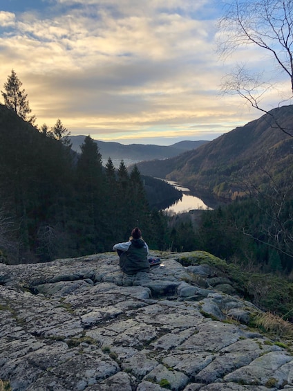 A person sitting on rocks overlooking a valley with a lake and mountains. 1