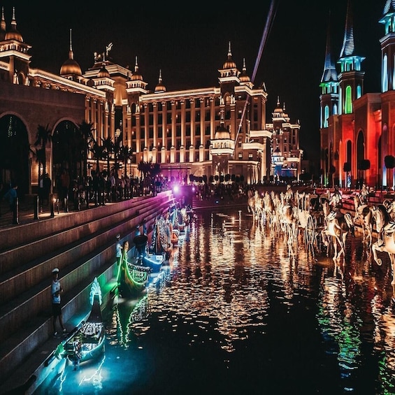 A nighttime view of a grand building with domed architecture, a canal with illuminated boats, and a fountain display. 4