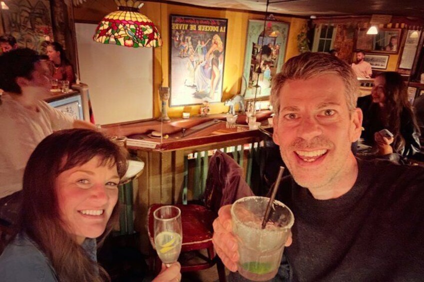 A person holding a drink with a straw, another person smiling, and a bar area with a poster in the background. 1