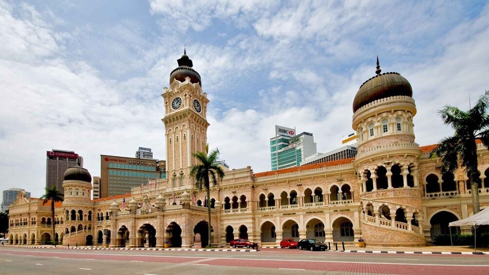 A historic building with two prominent towers, one with a clock, and a modern skyscraper in the background. 1