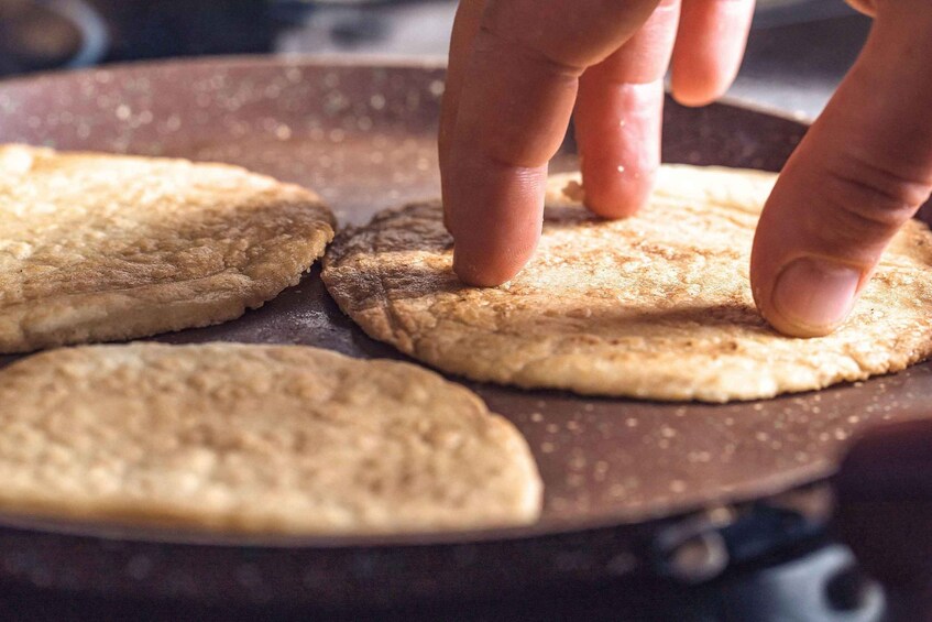 A hand pressing down on a flatbread in a pan. 5