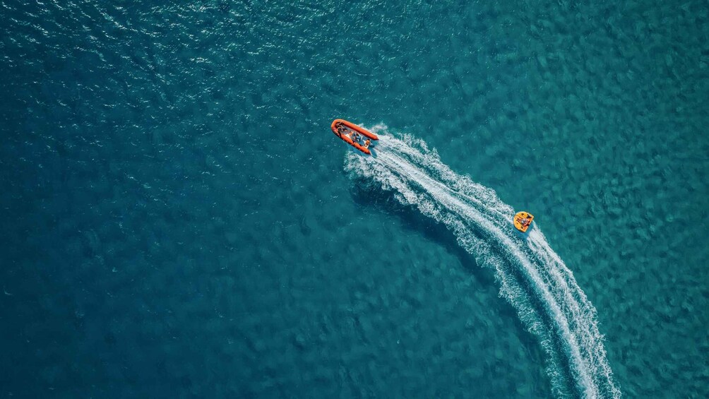 Two boats on a turquoise sea, one orange and one yellow, creating trails behind them. 2