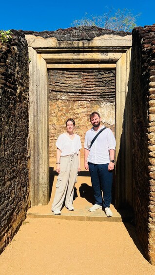 Two people standing in a doorway with a brick wall and a clear blue sky in the background. 2