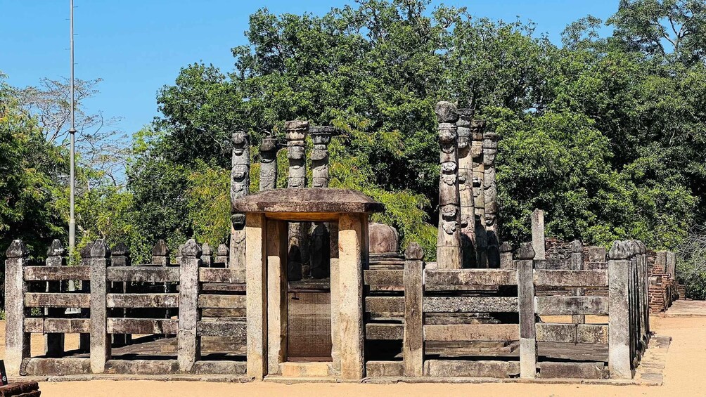 An ancient stone structure with a central doorway, flanked by stone columns and a wooden fence. 3