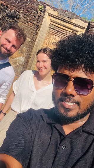 Three people outdoors near a stone wall and wooden structure. 4