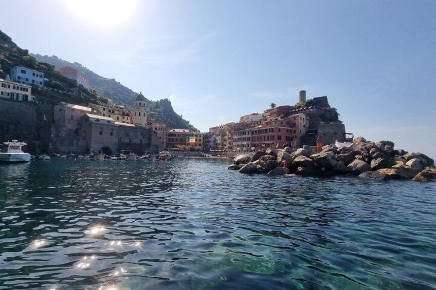 A coastal town with buildings along the water, clear blue water, and a rocky shoreline. 3