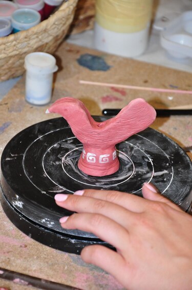 A hand holding a pink sculpture on a black rotating platform. 2