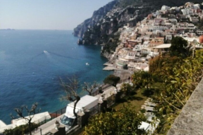 A coastal town with buildings along the cliffside, a body of water, and a vehicle on the road. 1