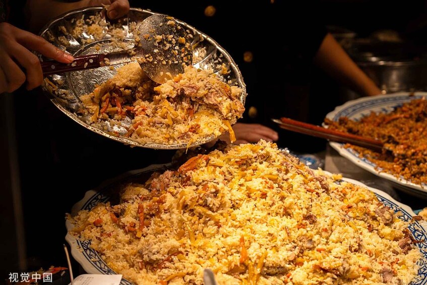 A person serving a large dish of rice with vegetables and meat. 4