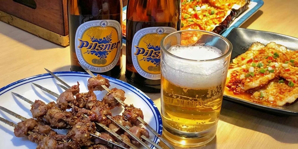 Skewered meat, beer bottles, a glass of beer, and a pizza on a table. 3