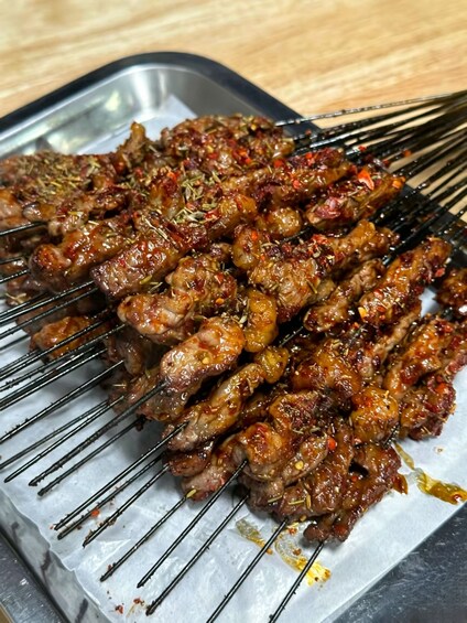 Skewered meat with visible herbs and spices, grilled on a metal tray. 2