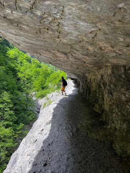 A person hiking on a rocky path with a cave entrance. 5