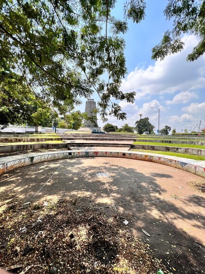 A park with a mosaic-tiled circular area, trees, and a distant monument. 5
