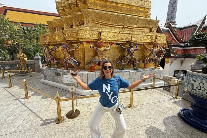 A person in front of a golden temple with statues, wearing a blue shirt and white pants. 1