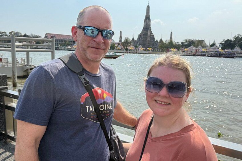 A man and a woman standing by a body of water with a temple in the background. 4